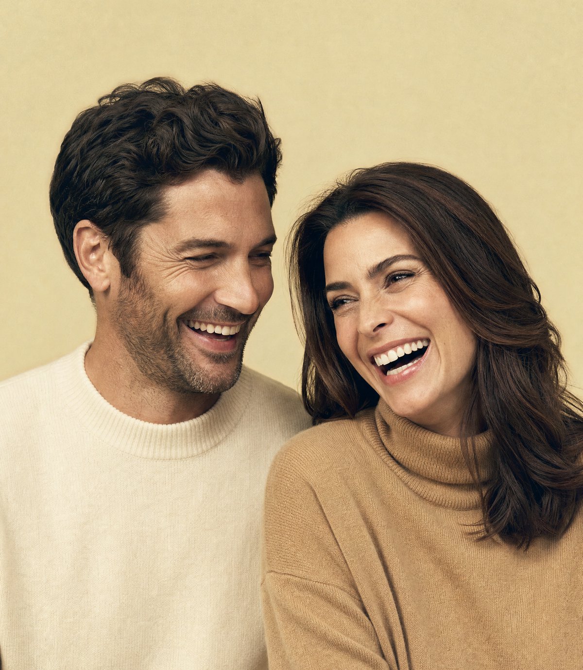 A man and a woman laughing together, both with full healthy hair, on a warm gold backdrop