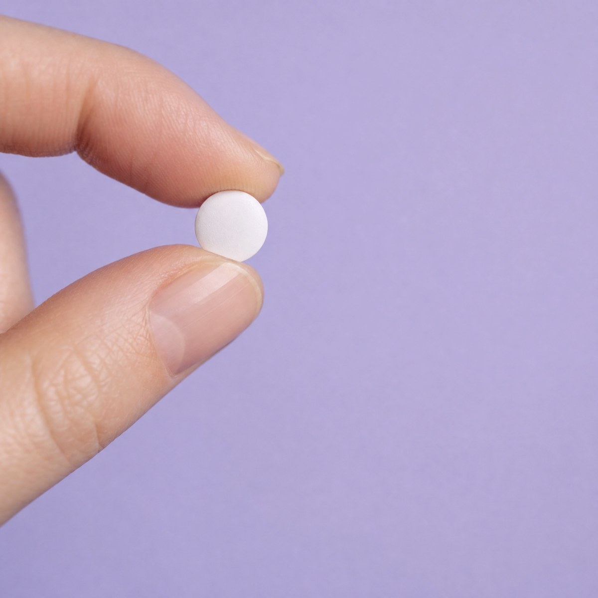 A fingertip holding a single small tablet in soft lavender light