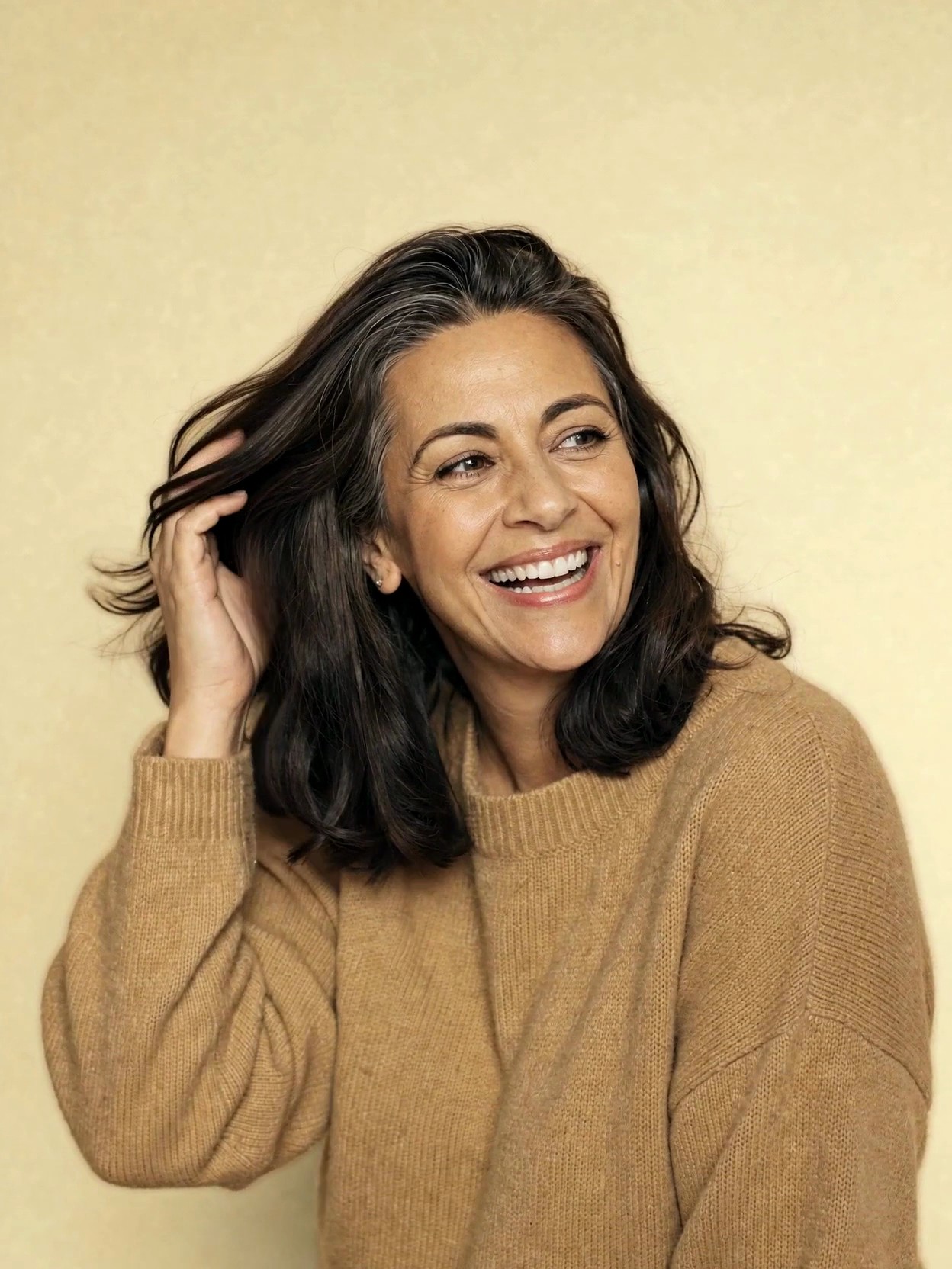 A woman in her late forties laughing warmly, her thick hair moving softly, on a warm gold backdrop