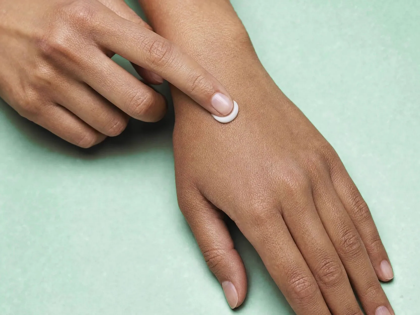 Overhead close-up of a fingertip spreading a small dab of cream across the back of a hand